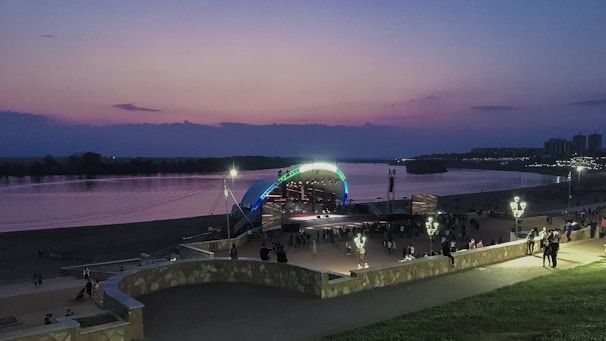 Crowd gathered near the river with a live band playing on an outdoor stage at sunset.