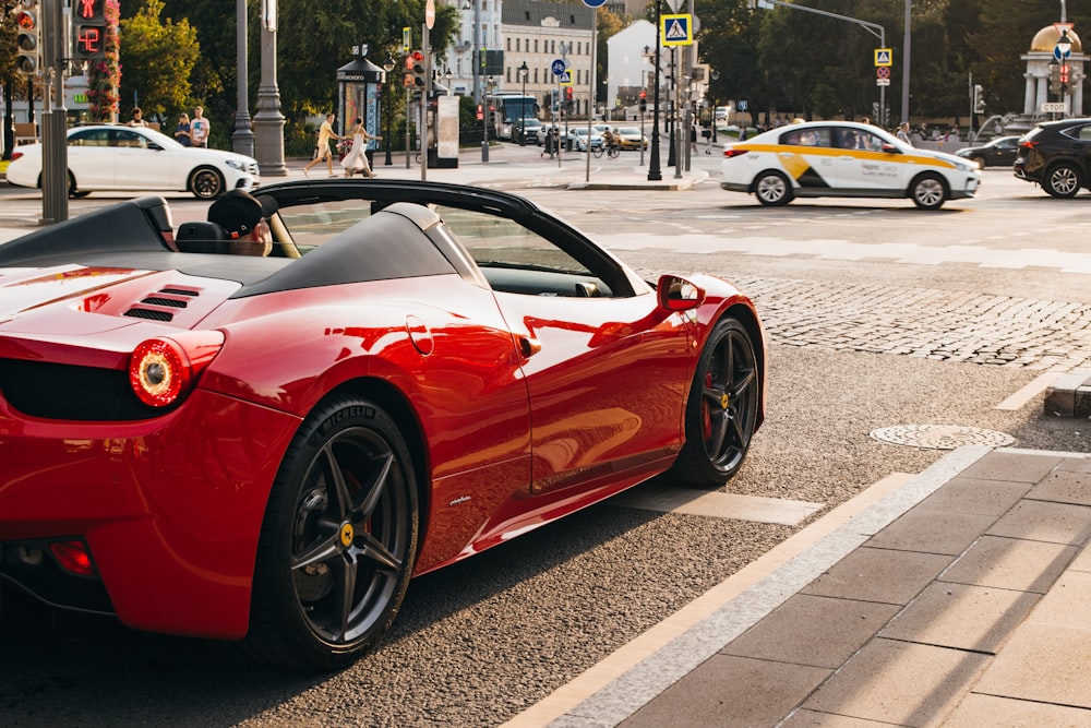 person sitting on the driver's seat of a red convertible coupe at the side of the road near cars on road during day