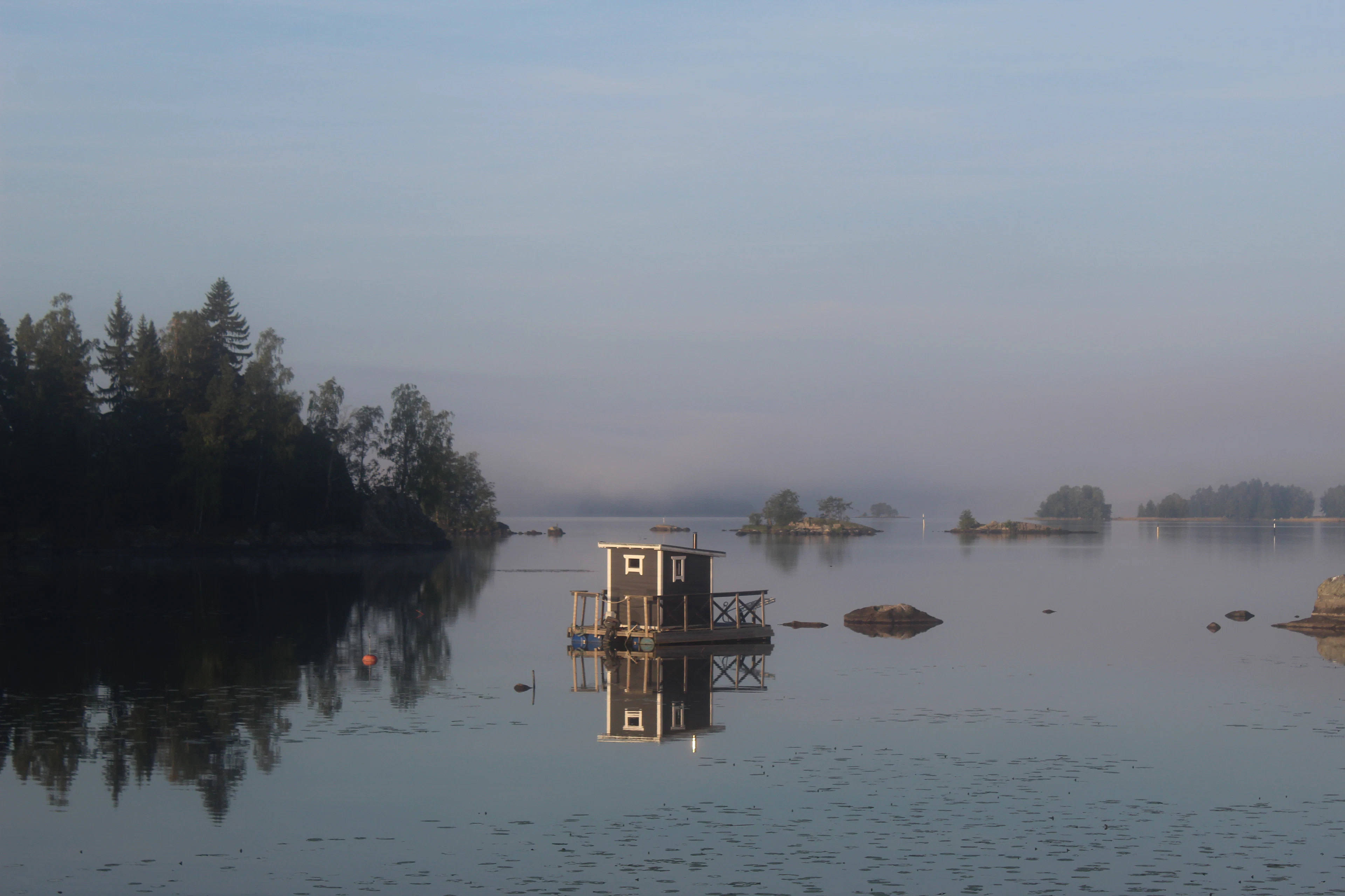 A small floating sauna on a calm lake in the morning mist, Finland