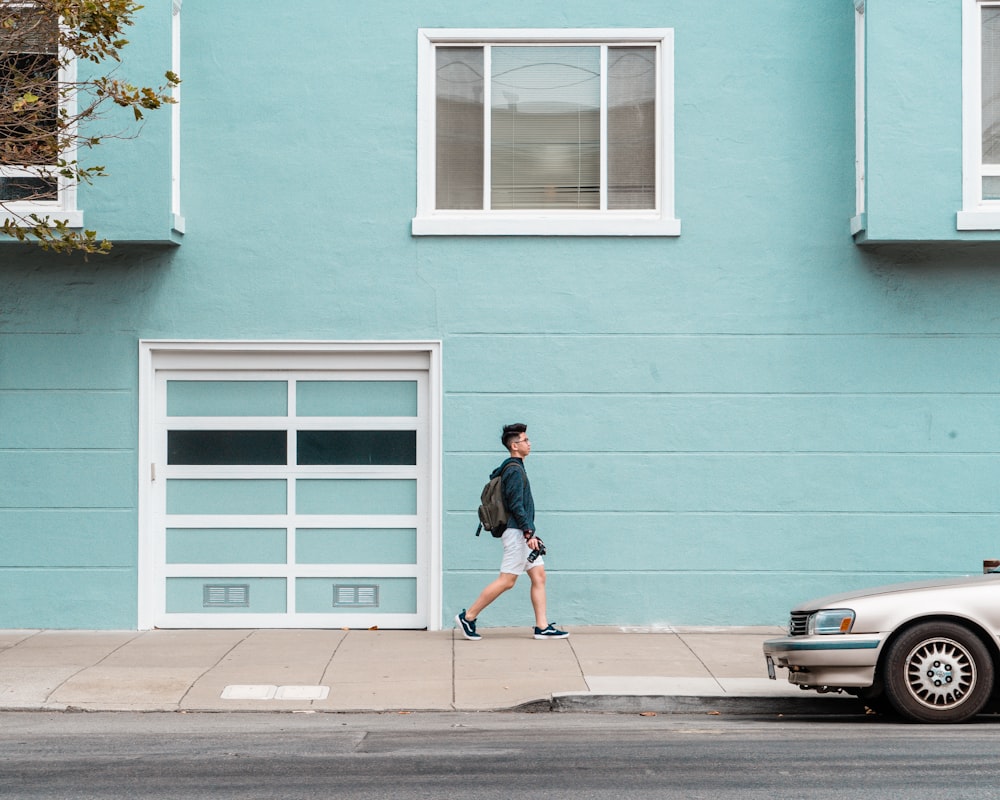 man walking outside house beside car