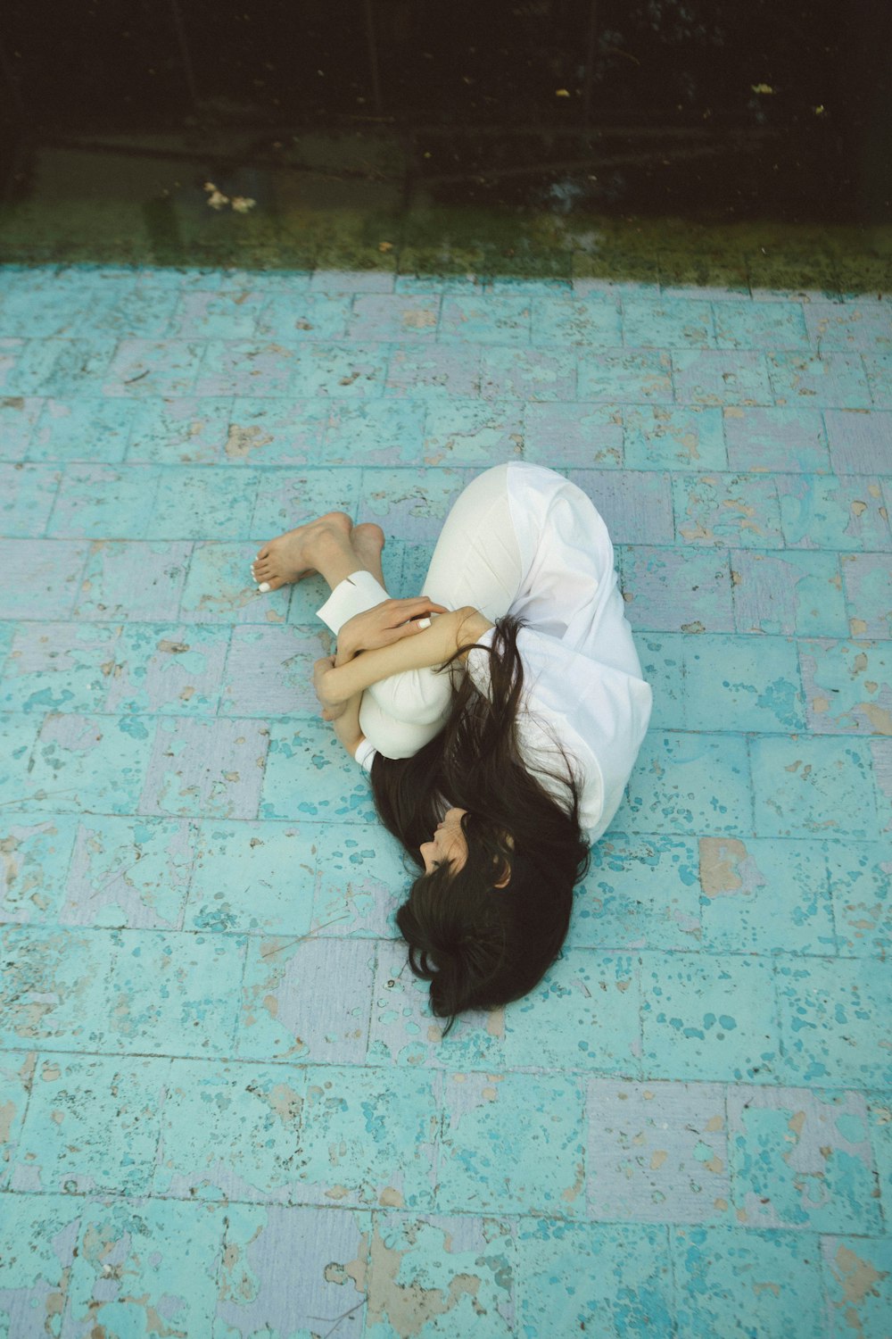 woman wearing white collared button-up long-sleeved shirt and pants lying on green concrete pavement
