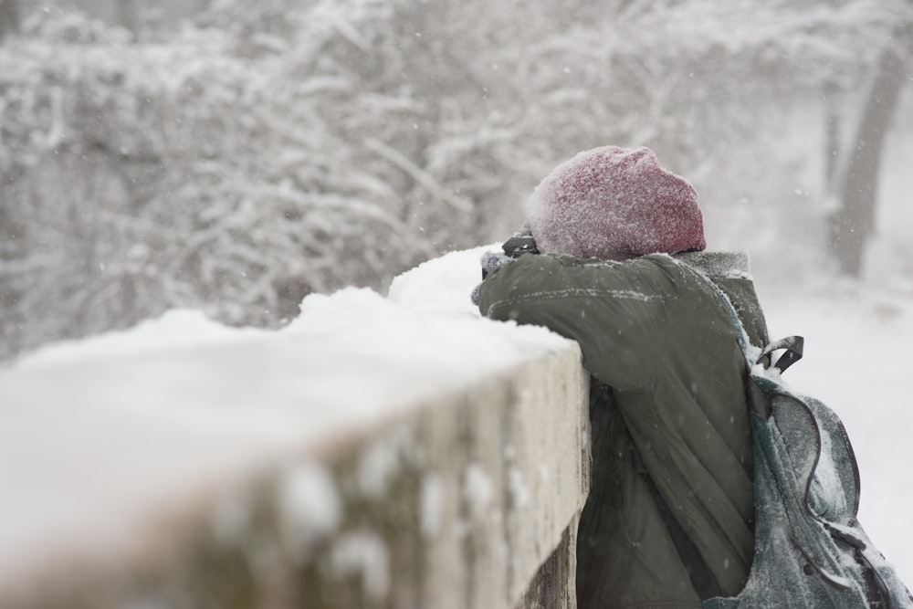 person leaning on a concrete wall covered in snow