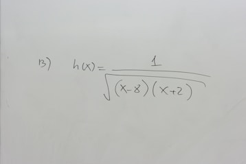 A section of a whiteboard features a mathematical expression written in black marker. The expression depicted is h(x) = 1 / √((x-8)(x+2)), which suggests a function involving variables and parentheses. The board is otherwise clean, with no additional markings or annotations.