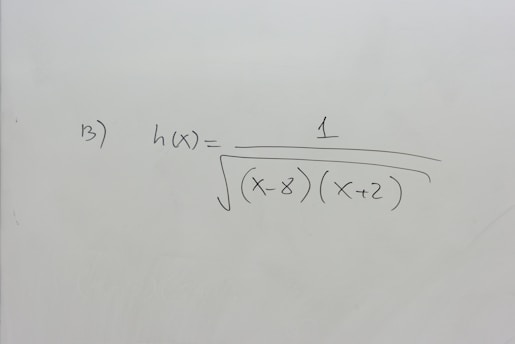 A section of a whiteboard features a mathematical expression written in black marker. The expression depicted is h(x) = 1 / √((x-8)(x+2)), which suggests a function involving variables and parentheses. The board is otherwise clean, with no additional markings or annotations.