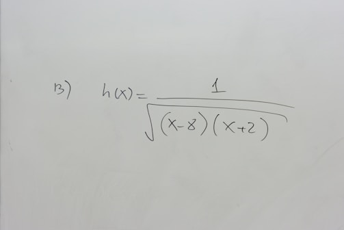 A section of a whiteboard features a mathematical expression written in black marker. The expression depicted is h(x) = 1 / √((x-8)(x+2)), which suggests a function involving variables and parentheses. The board is otherwise clean, with no additional markings or annotations.