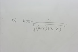 A section of a whiteboard features a mathematical expression written in black marker. The expression depicted is h(x) = 1 / √((x-8)(x+2)), which suggests a function involving variables and parentheses. The board is otherwise clean, with no additional markings or annotations.