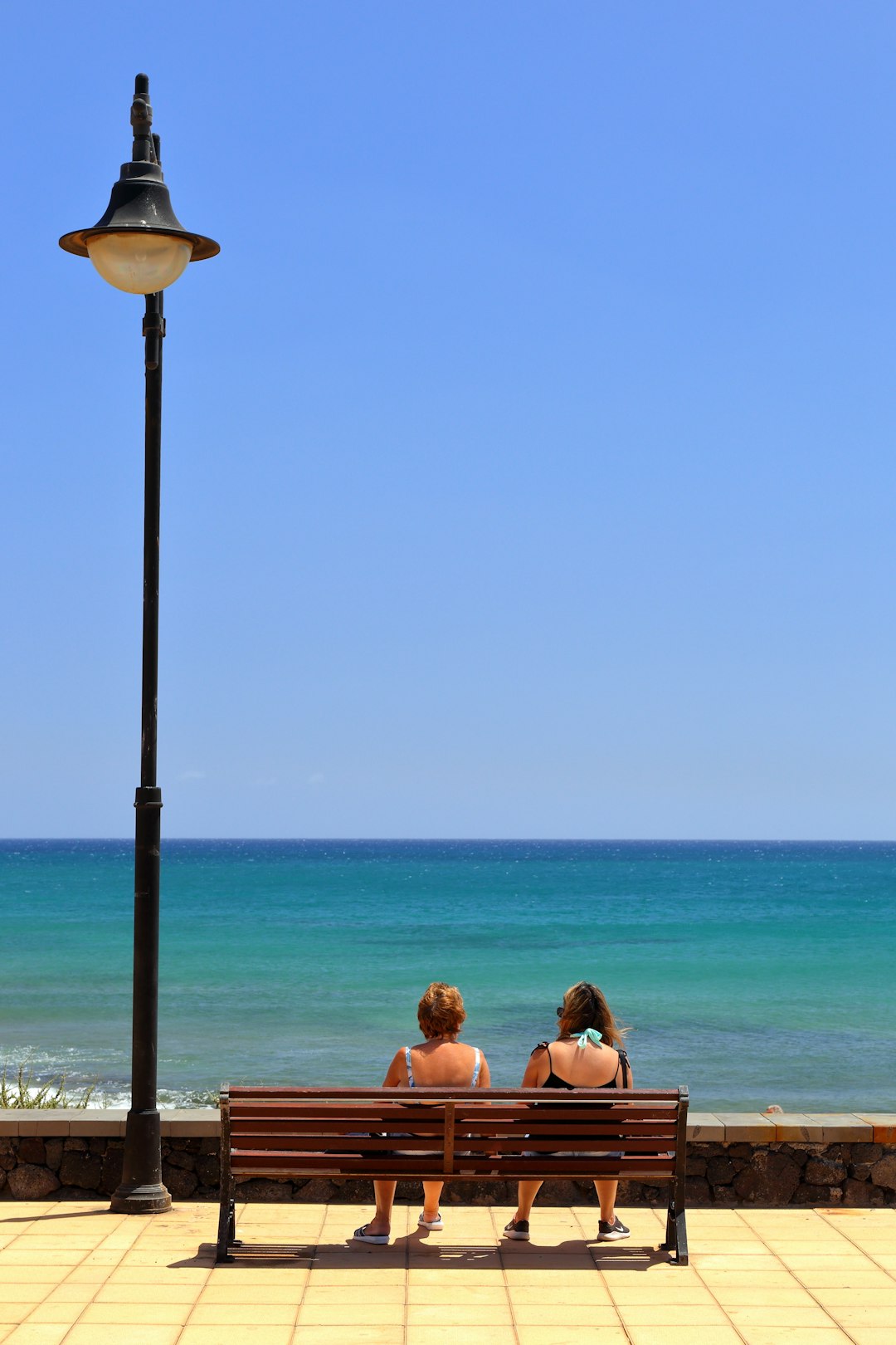 two women sitting on wooden bench front of sea