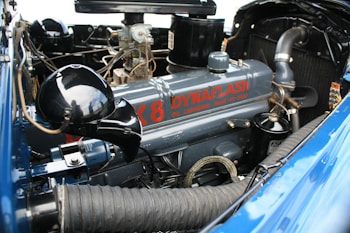 An antique car engine is detailed, showcasing an intricate mix of metal parts and tubes. The engine's casing is labeled 'DynaFlash', and the equipment has a vintage appearance with visible bolts and connections. The surrounding parts are primarily metallic, with a mix of black and blue components. Hoses and wiring are visible, highlighting the complexity and detail of the old mechanical design.