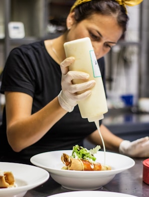 A skilled hand pouring rich sauce into a glass container under warm lighting.