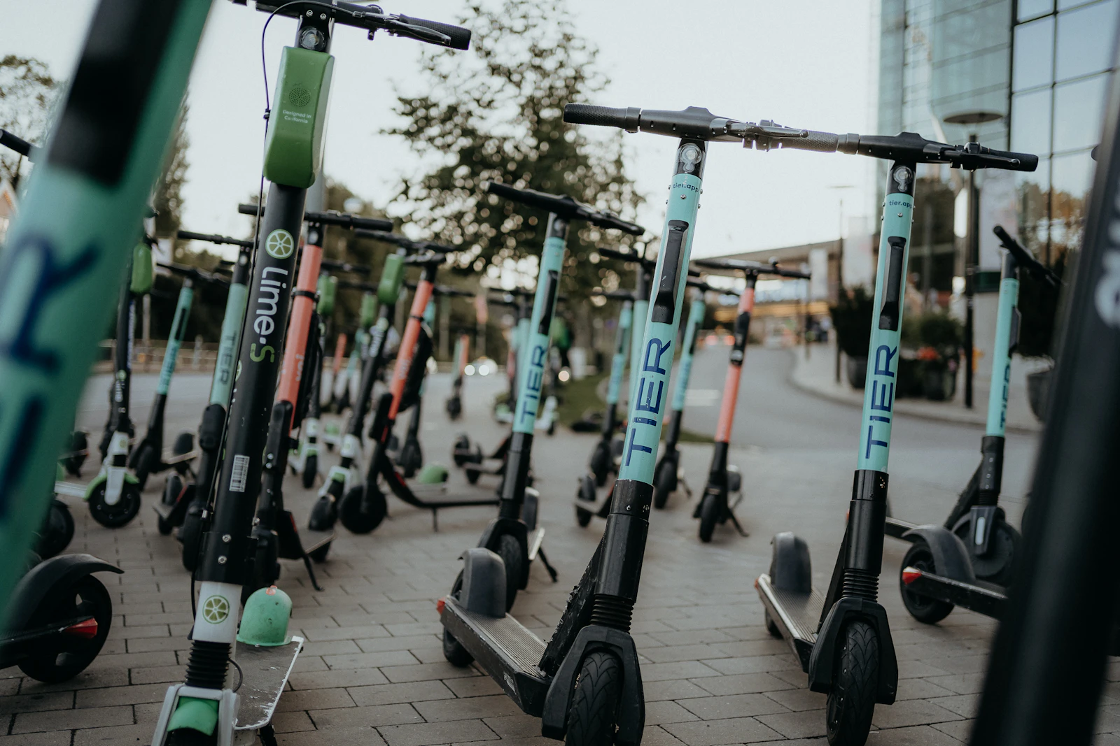 A row of shared electric rental scooters lined up on a city sidewalk downtown.