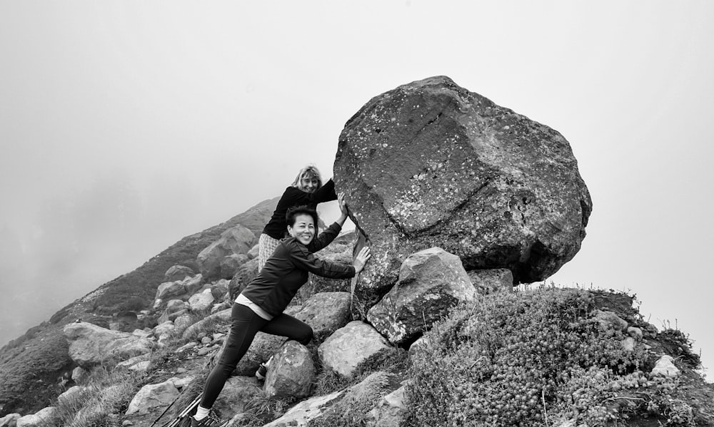 grayscale photography of two women pushing rock