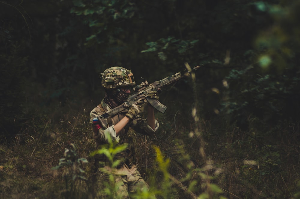 man pointing assault rifle near trees