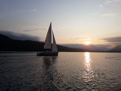 Elegant sailboat gliding over the tranquil deep blue waters of Lake Maggiore at sunset.