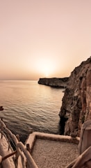 A serene Mediterranean coastal path at sunset with soft pastel skies.