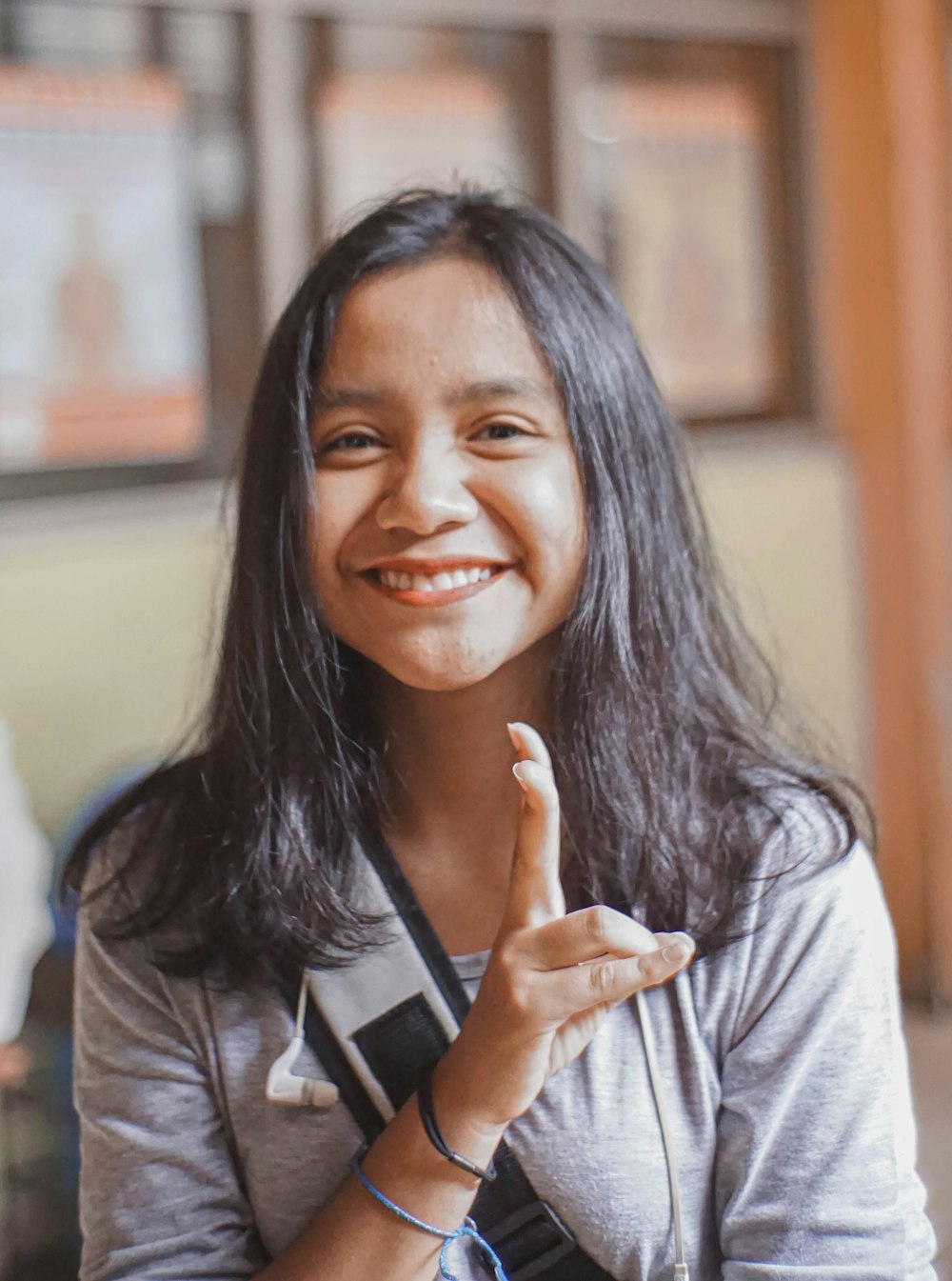 woman wearing gray crew-neck t-shirt smiling while making peace hand sign