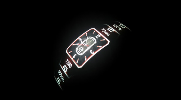 A digital smartwatch display is illuminated against a dark background. The screen features a digital clock with both analog and digital formats, including health metrics like step count, heart rate, and calorie count.