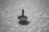 A spinning top is in motion on a textured surface, casting a shadow beneath. The image is in black and white, highlighting the smooth, circular movement of the top.