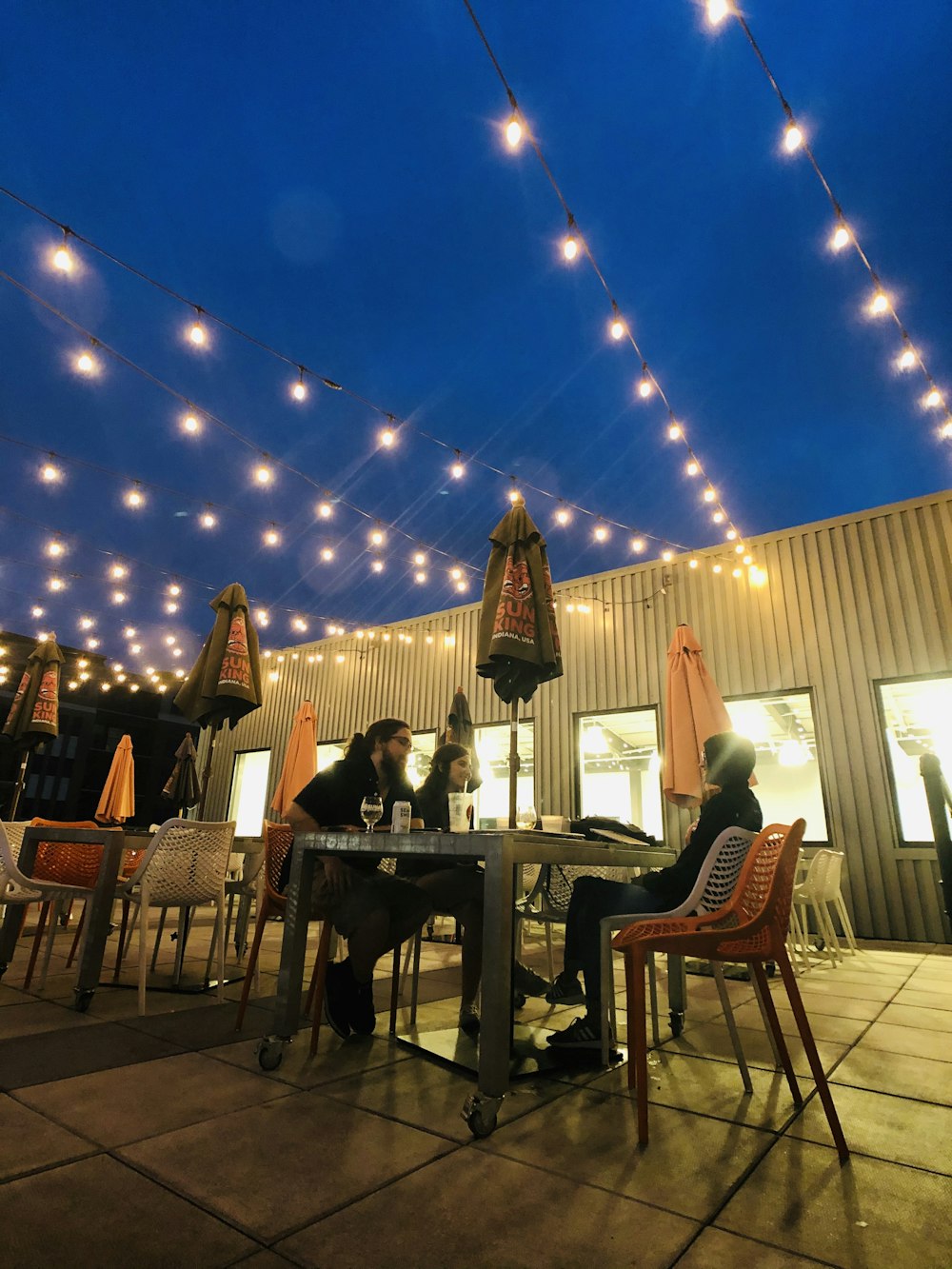 people sitting on outdoor table under string lights during night time