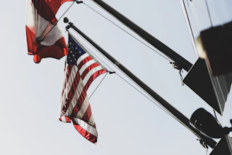 Close-up of Canadian and American flags on metal poles waving side by side.