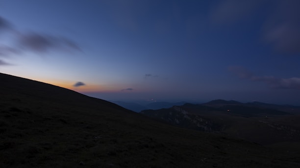 A serene landscape at dusk, with a silhouette of a person standing on a hill, gazing at the horizon.
