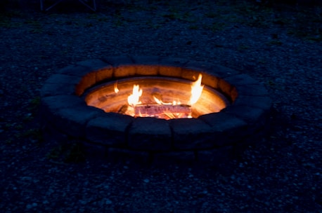 A custom stone firepit glowing warmly in an outdoor living space at dusk.