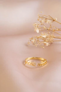 A warm gold ring catching the light, placed on a rustic wooden table surrounded by tiny wildflowers.