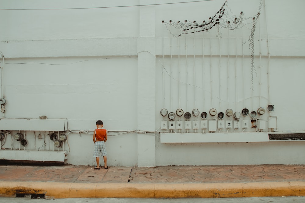 boy in orange by a white cement wall