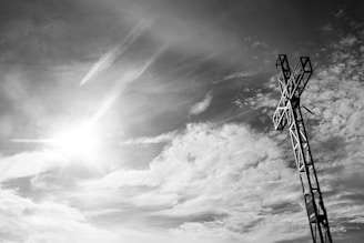 A sunlit cross standing tall against a vibrant blue sky with soft clouds.