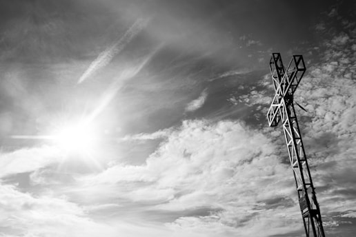 A sunlit cross standing tall against a vibrant blue sky with soft clouds.