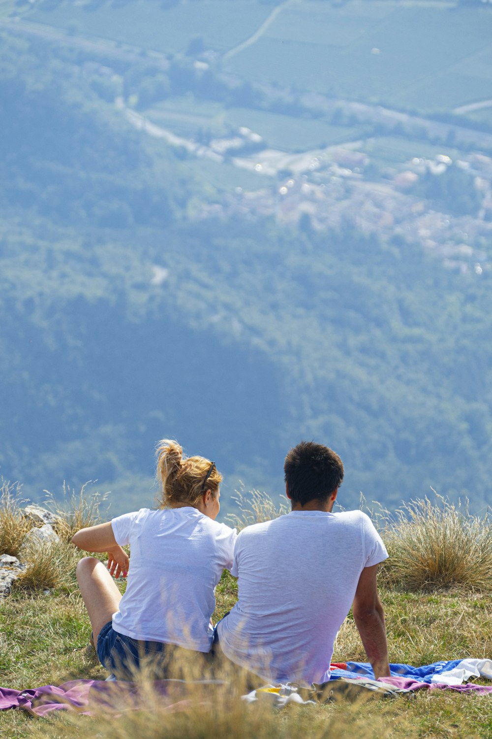 man iand woman in white shorts sitting on hill