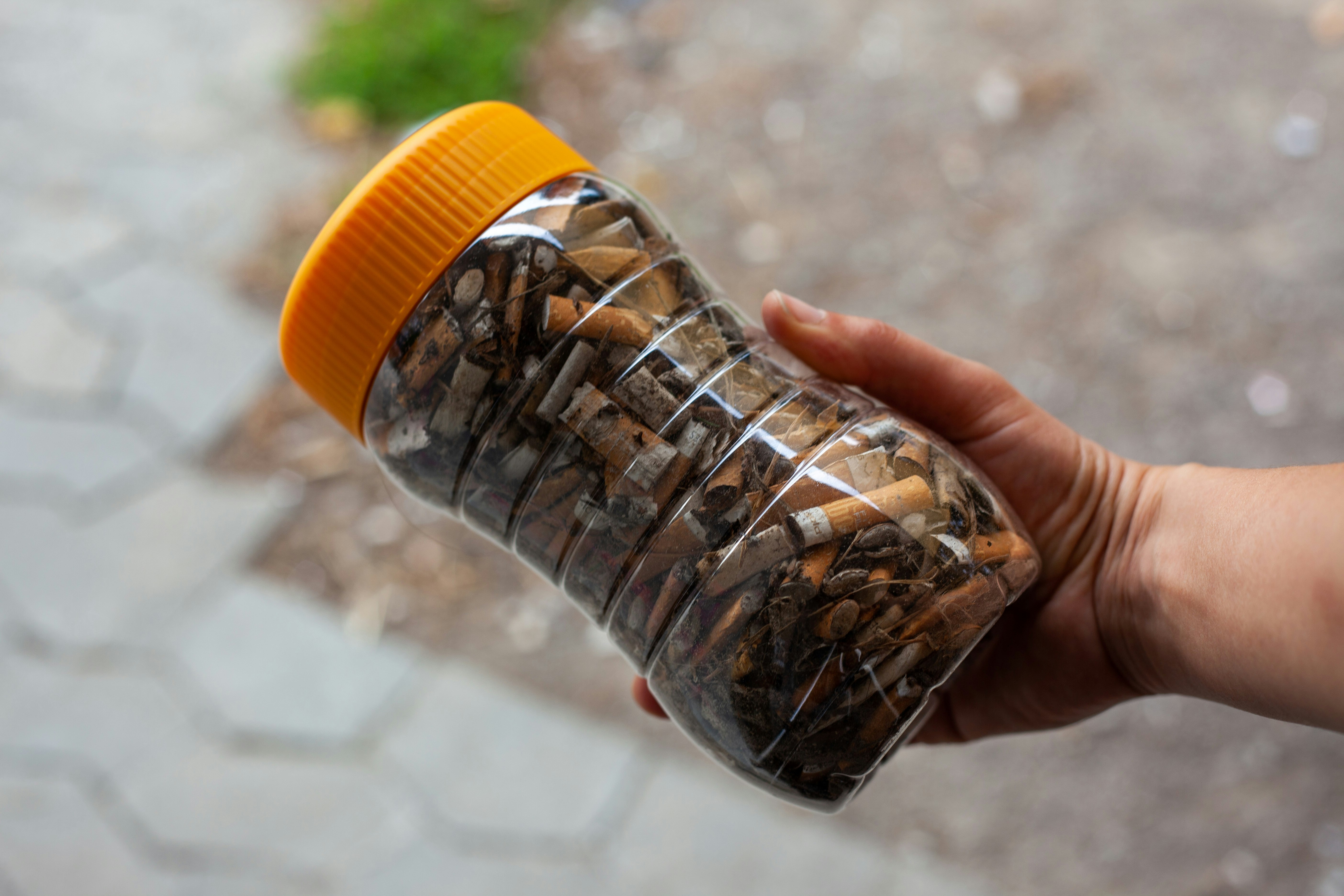 person holds jar of cigarette butts