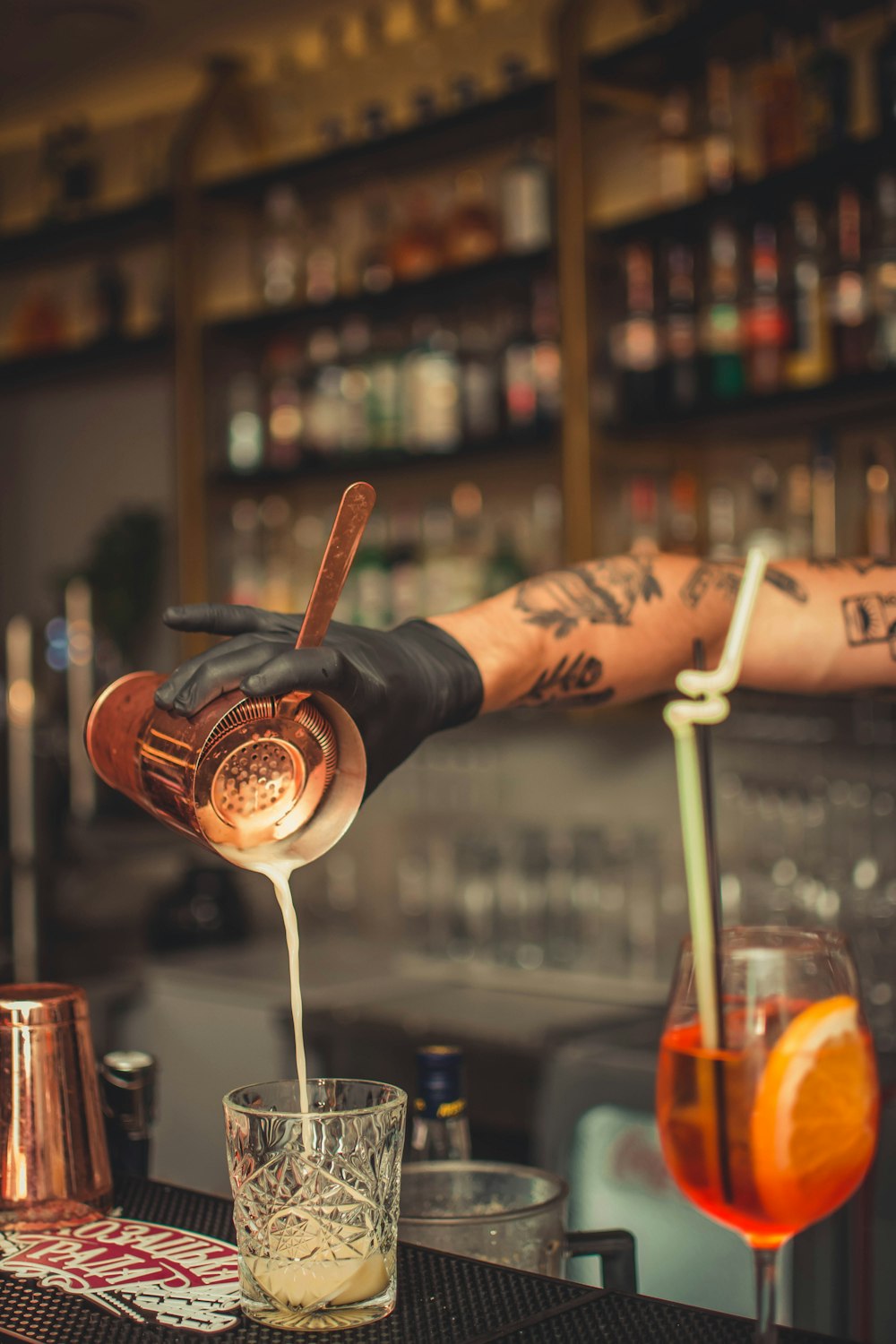 person pouring brown liquid into clear cut-glass shot glass inside bar