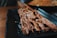 Skewered pieces of grilled meat, likely beef or lamb, are arranged on a black rectangular plate. The meat is lightly garnished with sesame seeds and appears juicy and well-cooked. The background includes a blurred view of more food in a round dish.