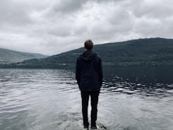 man standing and facing on river under white skies during daytime