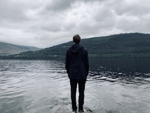 man standing and facing on river under white skies during daytime
