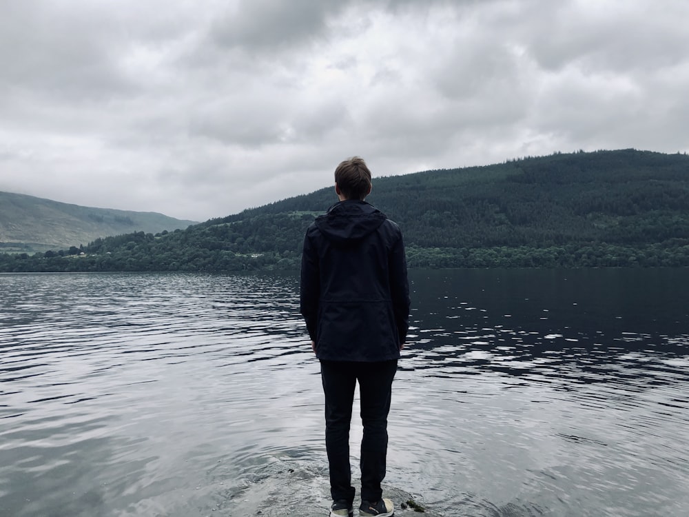 man standing and facing on river under white skies during daytime