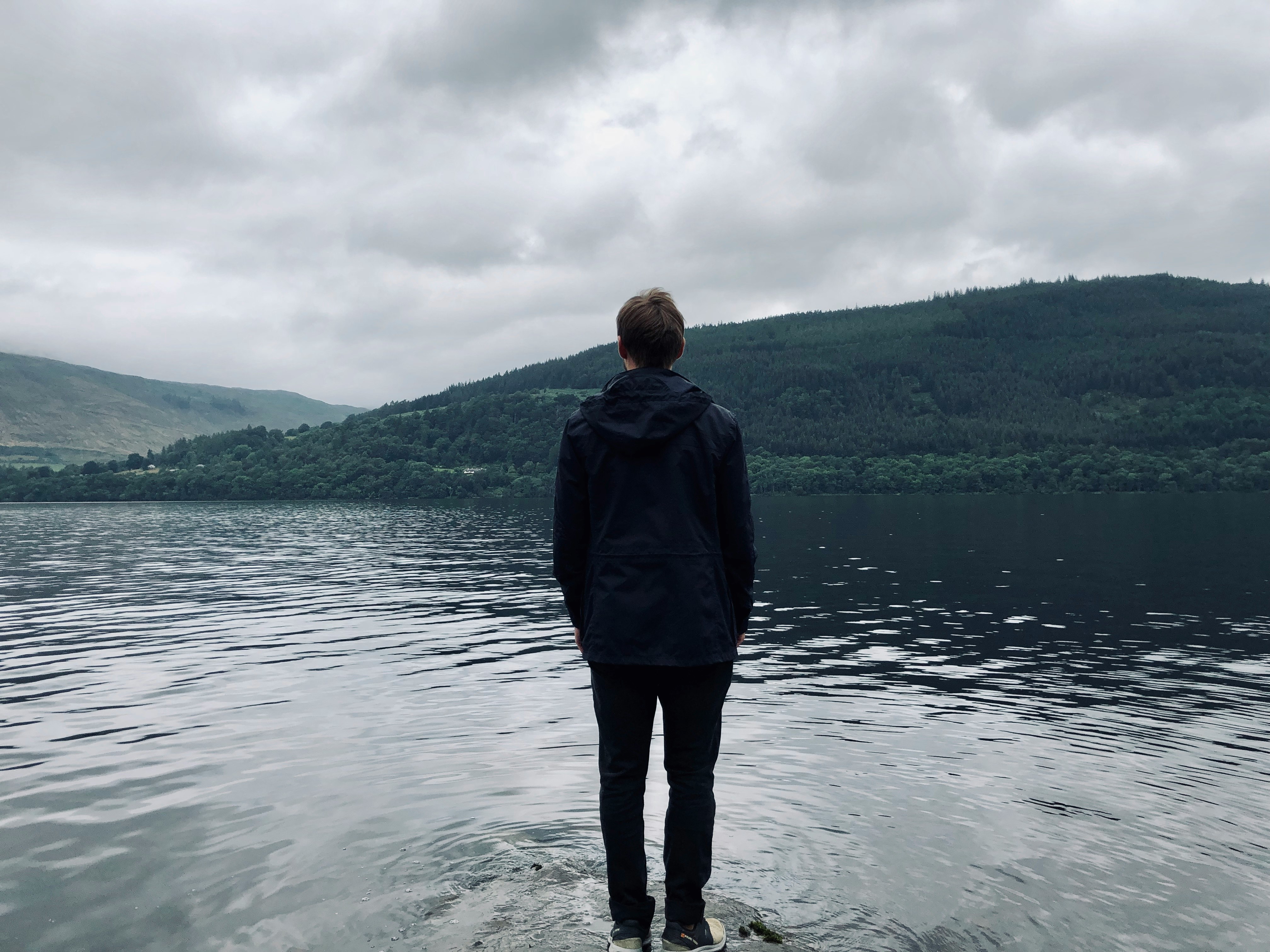 man standing and facing on river under white skies during daytime