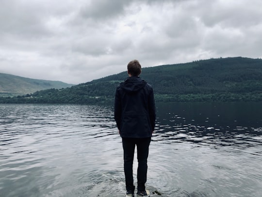 man standing and facing on river under white skies during daytime in Loch Tay United Kingdom