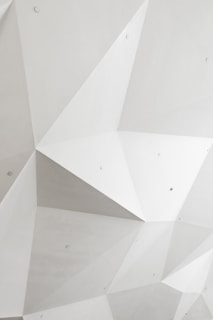 Geometric pattern featuring large, angular facets with a minimalist design. The surface is predominantly smooth and light-colored, with subtle shadows highlighting the 3D structure.