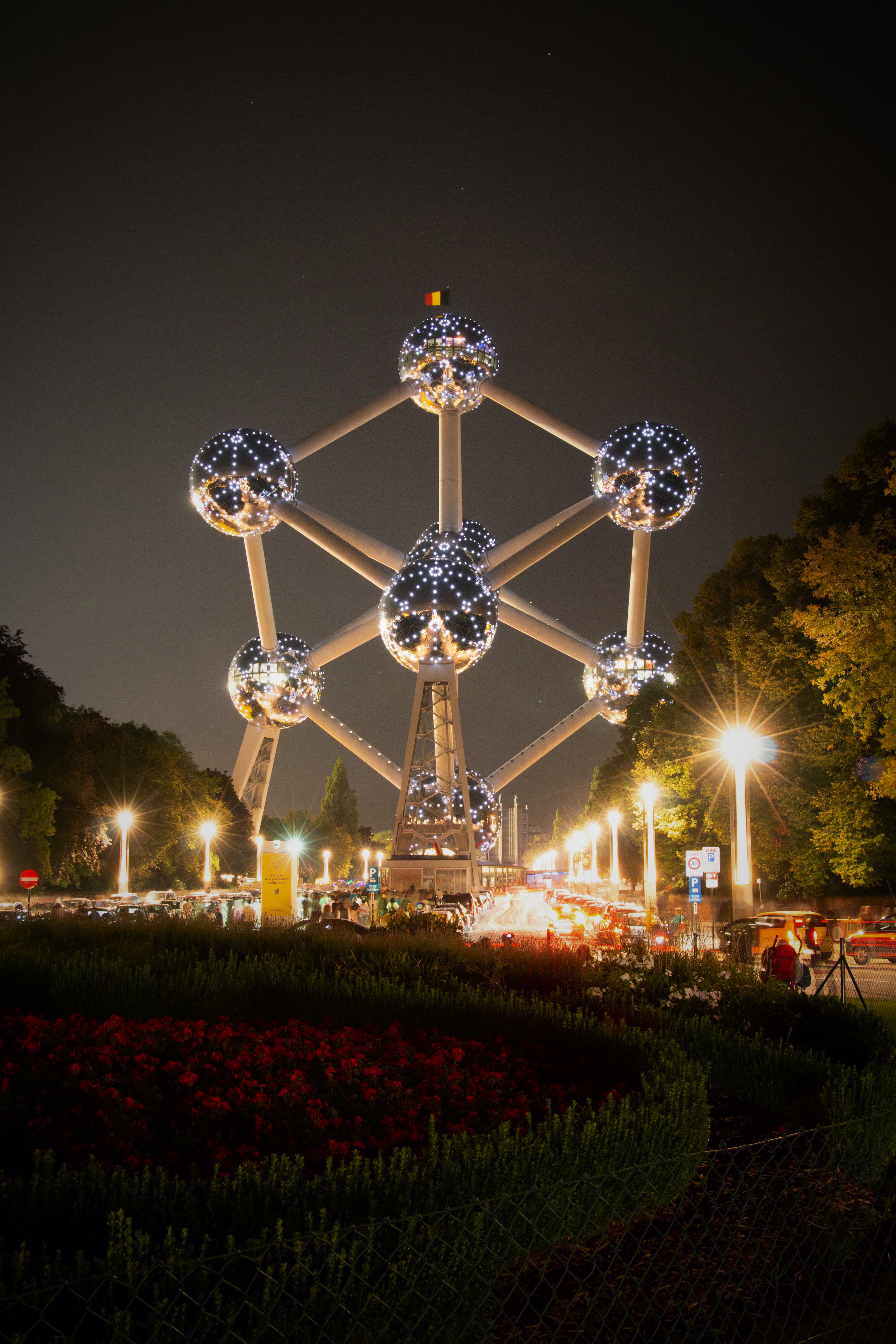 The nine steel spheres of the Atomium lit up at night above flowerbeds and street lamps in Brussels