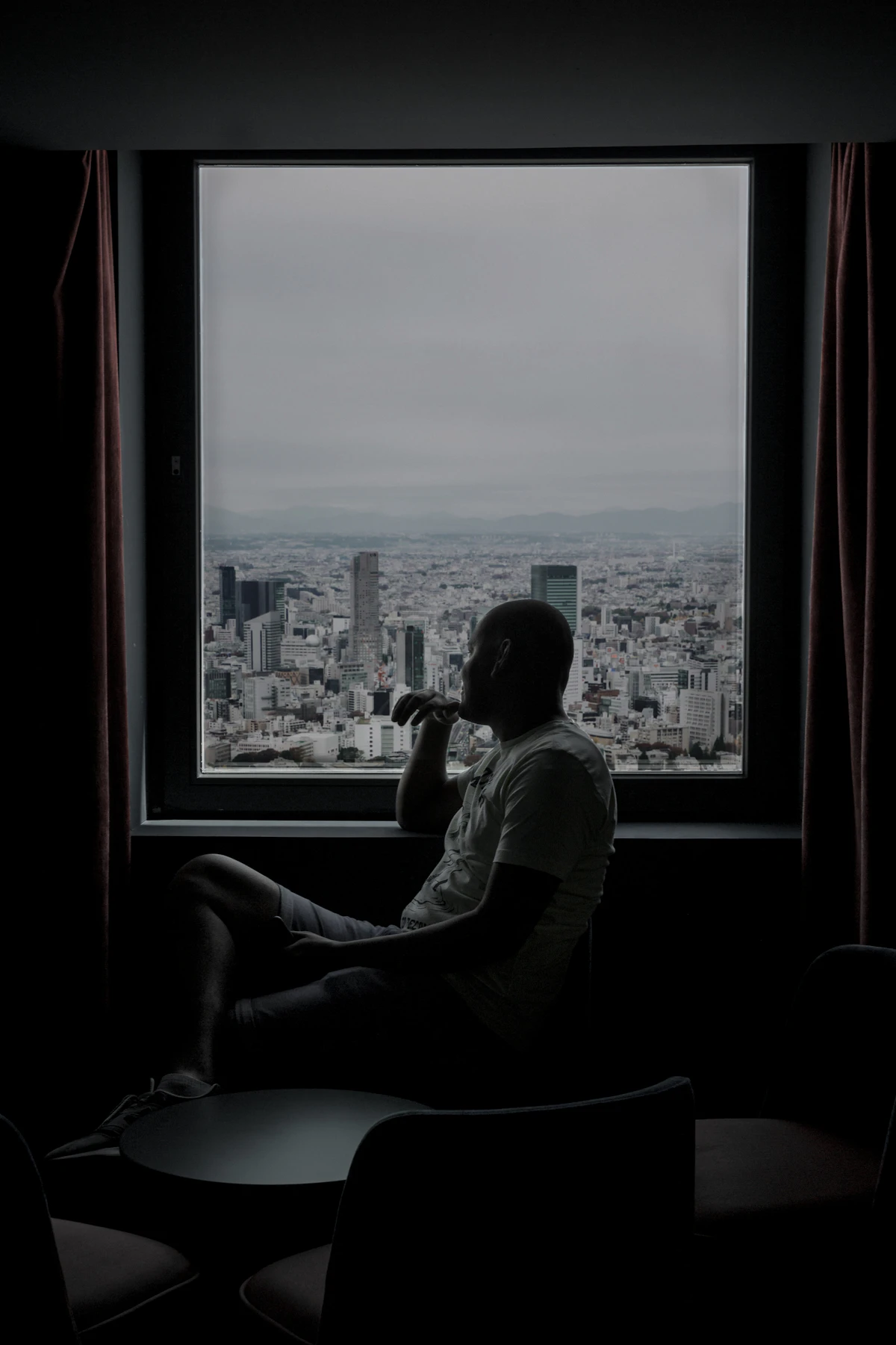 Silueta de un hombre bebiendo solo junto a una ventana con vistas a la ciudad de noche