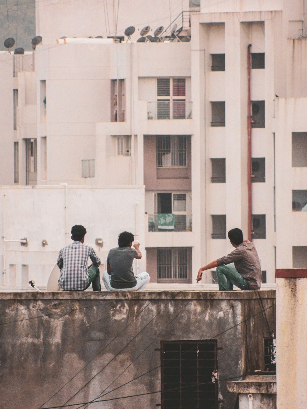 three men sitting on top of building during daytime
