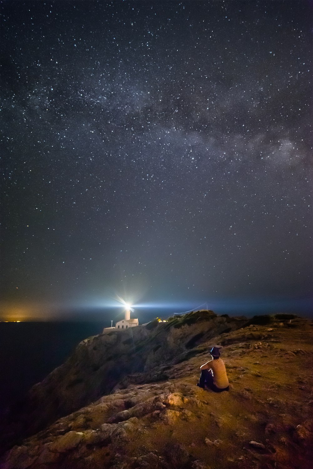person sitting near cliff under starry night