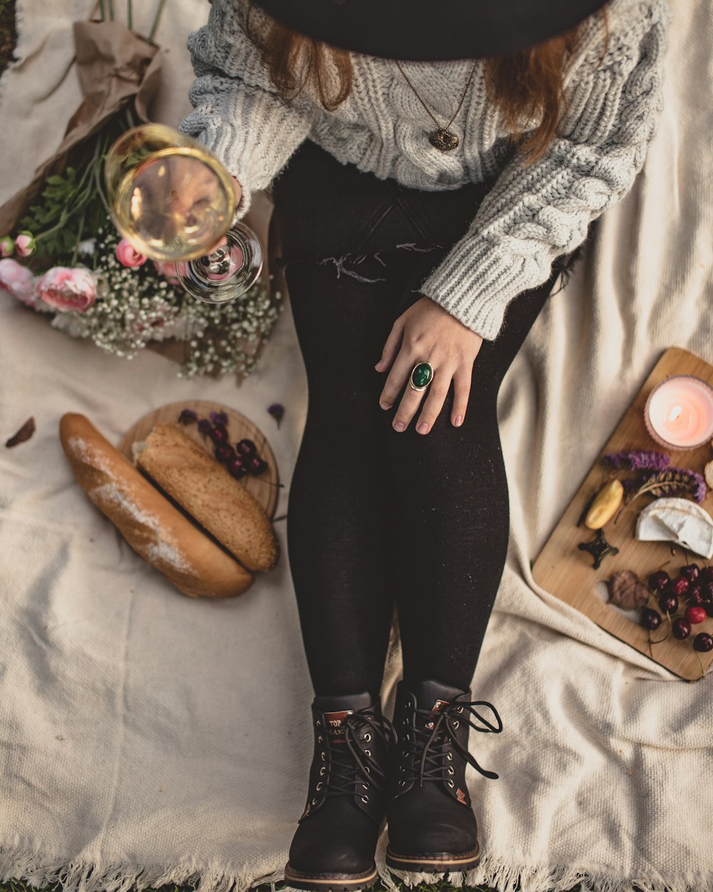 a woman in black boots and a hat sitting on a blanket