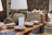 A rustic interior setting features a collection of woven baskets stacked neatly in the background, accompanied by a selection of decorative ceramic bowls placed on a wooden table. A large, textured table lamp with a beige shade casts light over the scene, contributing to the warm ambiance. Artwork and a patterned textile decorate the walls, enhancing the room's artisanal feel.