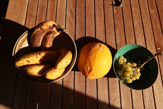 A rustic wooden table with fresh bananas and mangoes beside a handwritten note and a pen.