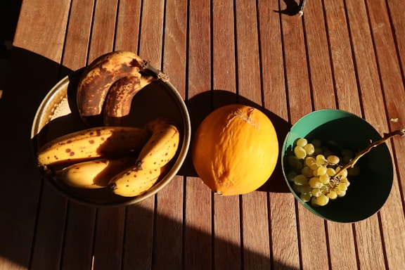 A rustic wooden table with fresh bananas and mangoes beside a handwritten note and a pen.