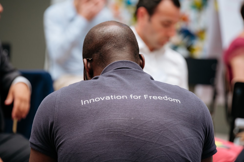 man wearing gray innovation for freedom print collared shirt near people