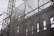 A black and white image of a construction site featuring a facade of a classical building being supported by scaffolding. The intricate architectural details of the building are visible through a translucent mesh, providing a contrast between the old-style architecture and the modern construction framework.