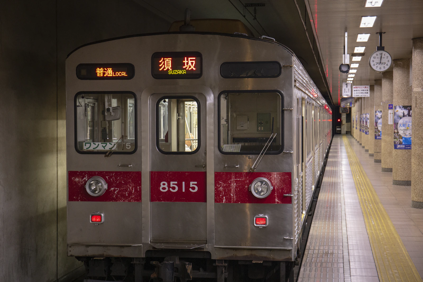 Photograph of local train waits at an underground platform with yellow tactile paving.